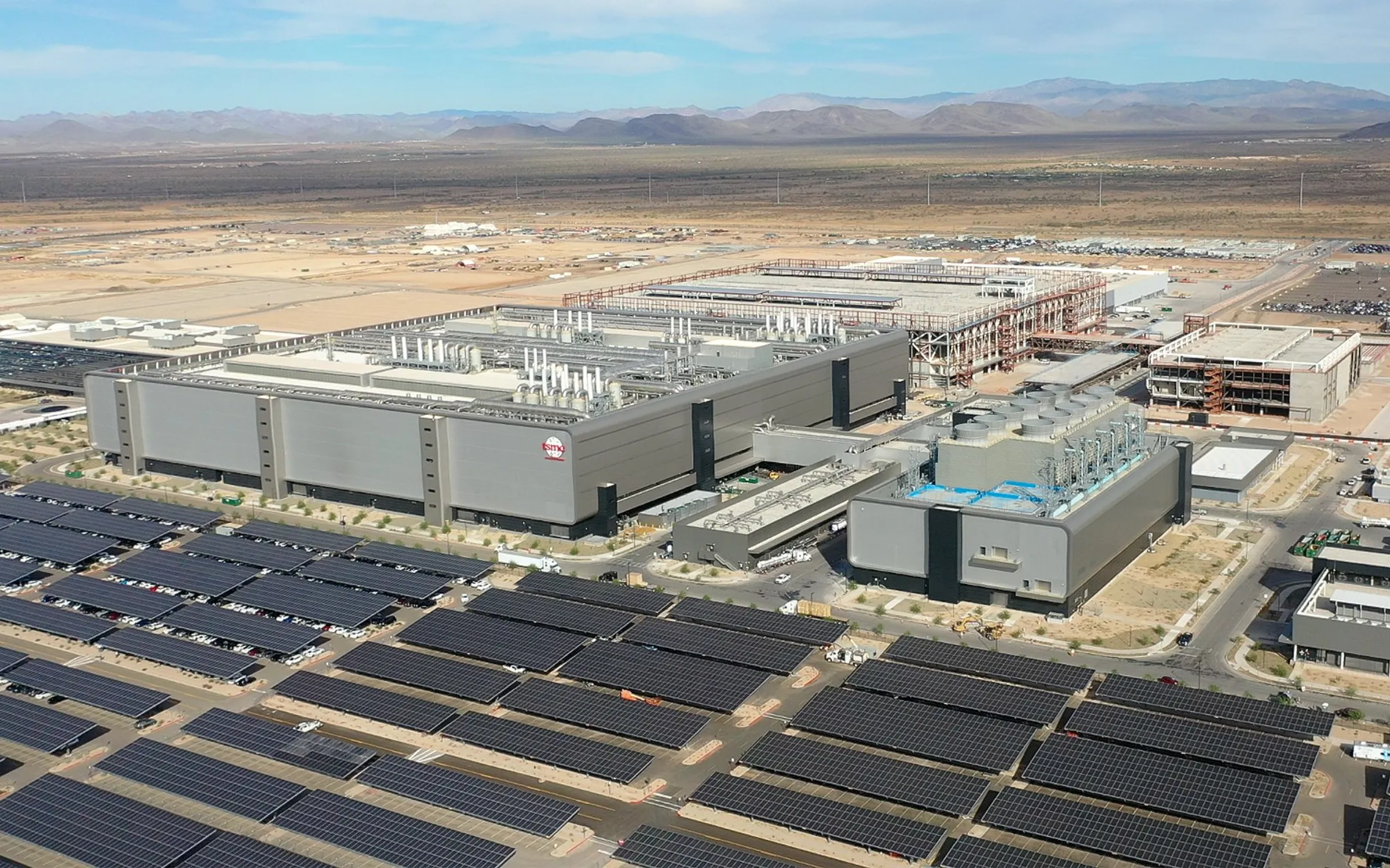 aerial photo of a manufacturing facility in desert landscape with field of solar panels in the foreground large buildings in th